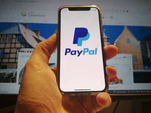 Smartphone mit PayPal-Logo vor Bildschirm, der Geestland-Homepage anzeigt