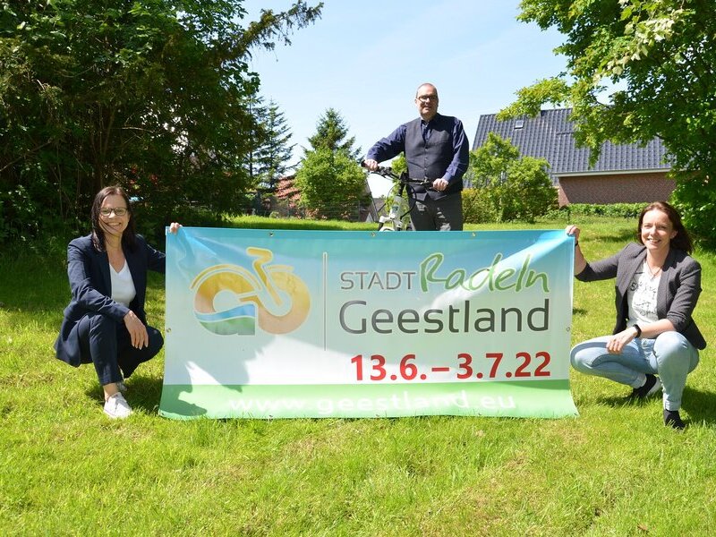 Sonja Thomas, Thorsten Krüger und Dana Hebener stehen mit einem STADTRADELN-Banner auf einer grünen Wiese